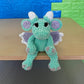 Crochet dragon toy in plush green chenille yarn with mauve and white highlights